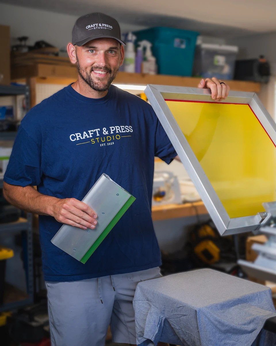 Bob Ingalls holding a squeegee next to his screen printing press in the Craft + Press studio