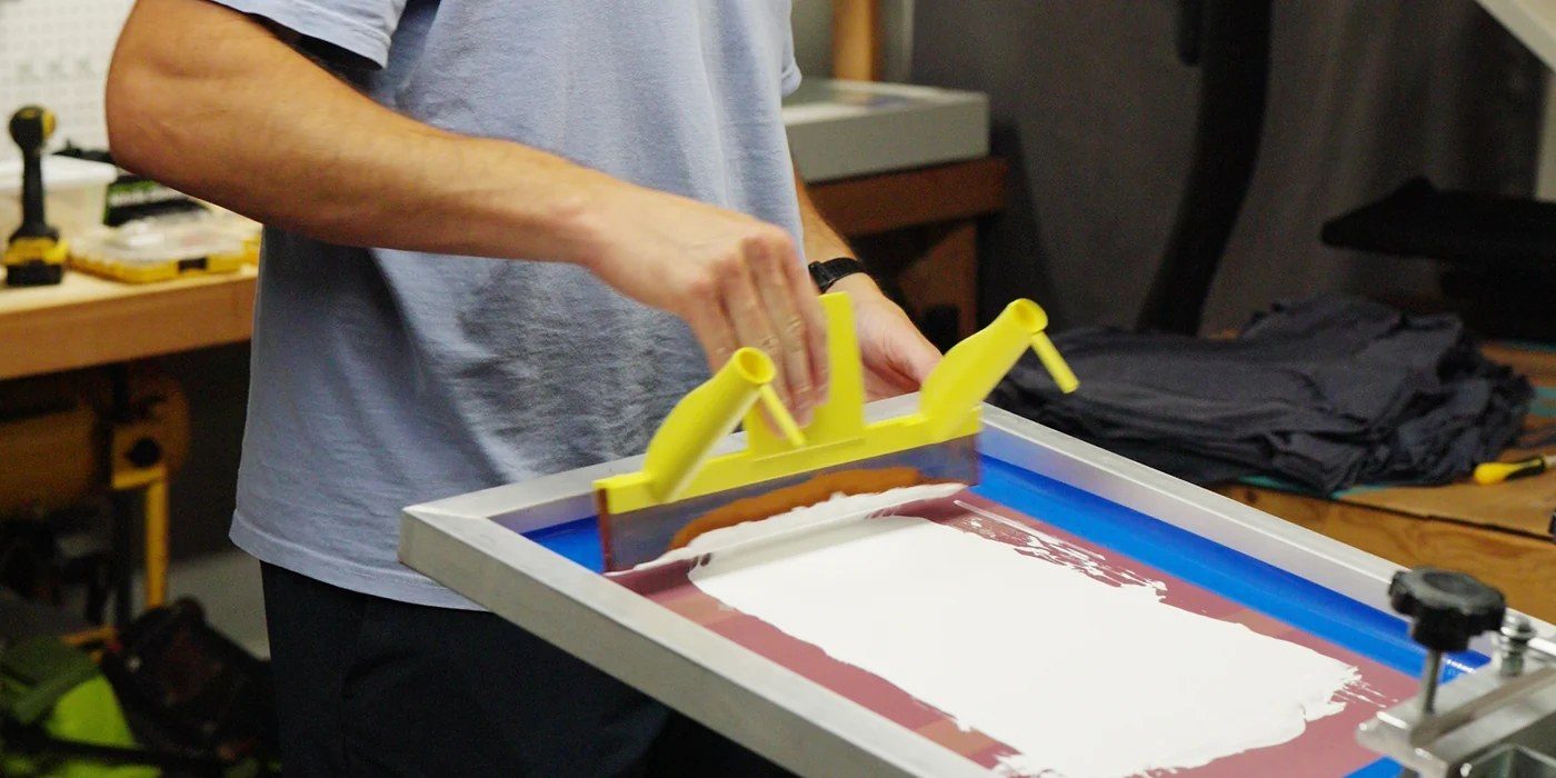 Close-up of hands pulling a yellow squeegee across a screen while printing the Golden Hour Yoga & Wellness job