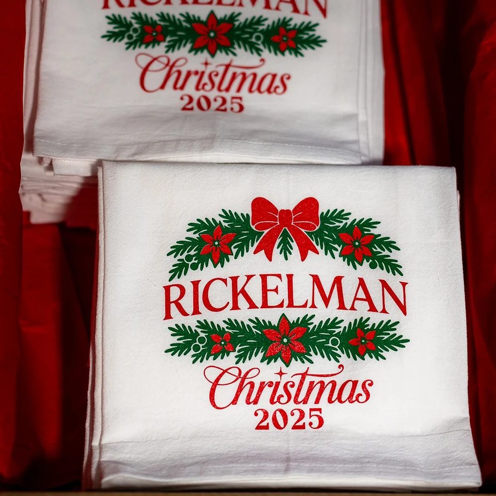 Stack of white towels printed with a red and green Rickelman Christmas design